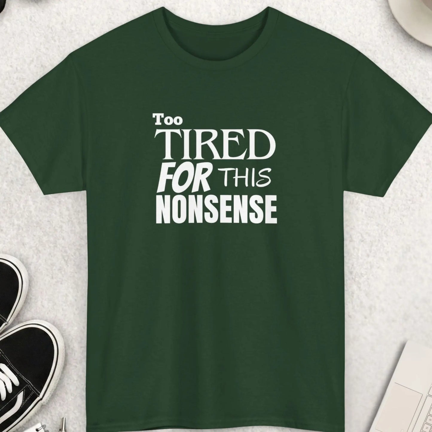 Green t-shirt with 'Too Tired for This Nonsense' text on a light gray surface with accessories.