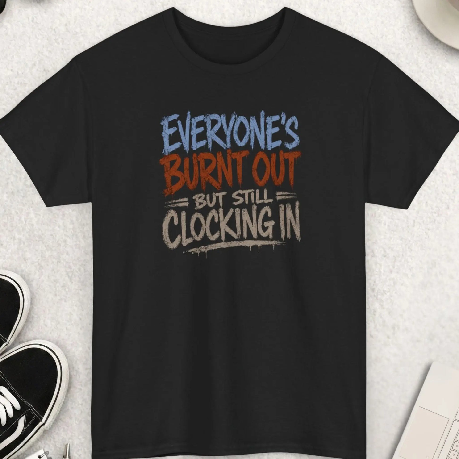 Distressed dark humor typography t-shirt reading “Everyone’s Burnt Out But Still Clocking In” in gray and burnt orange brush lettering on a black shirt with grunge streetwear aesthetic.