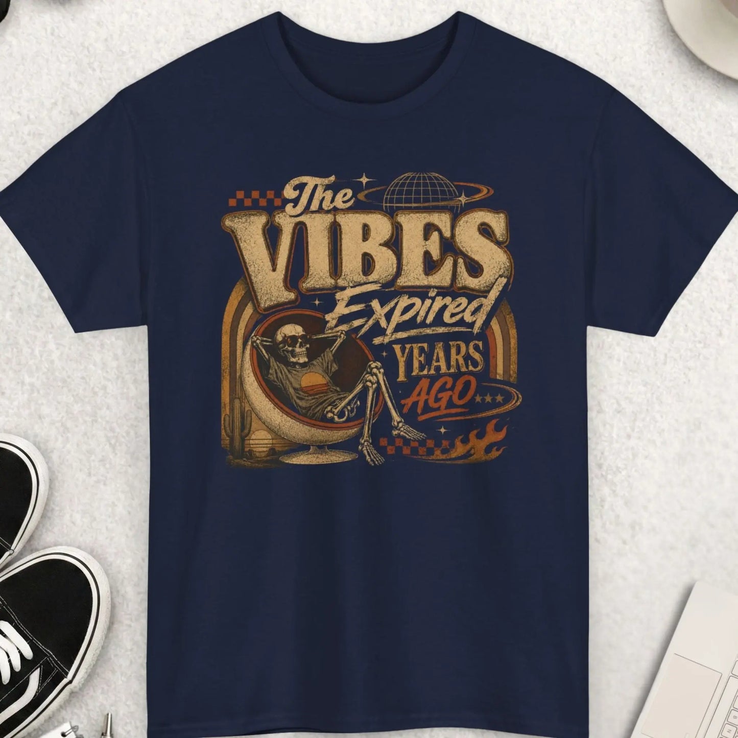 Navy blue vintage streetwear graphic tee featuring distressed typography reading “The Vibes Expired Years Ago” with retro desert artwork and a lounging skeleton in a surreal cosmic setting.