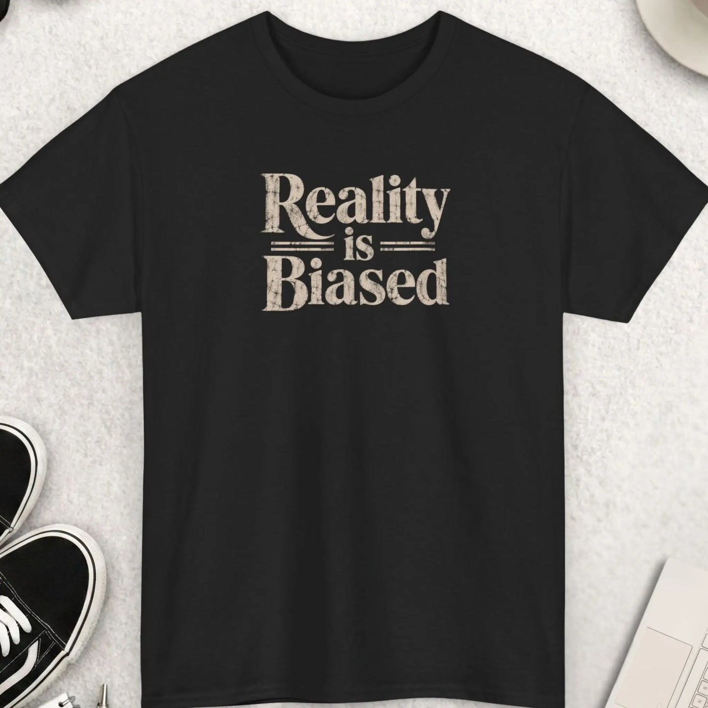 Black t-shirt with distressed bold typography reading “Reality Is Biased” in large vintage-style lettering