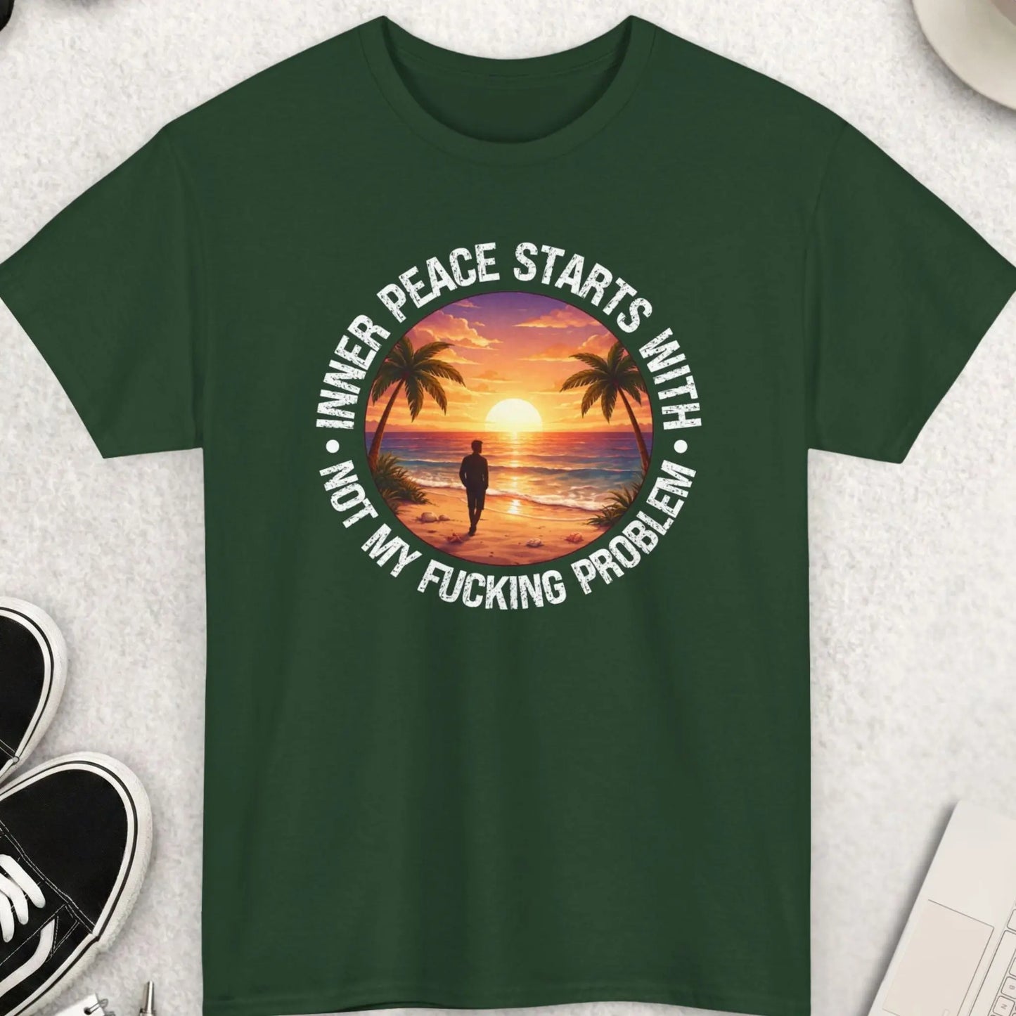 Green t-shirt with a sunset design and text on a light gray surface with accessories.