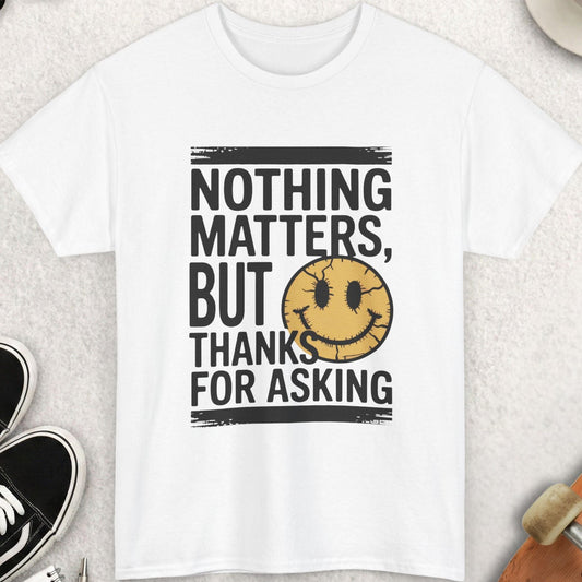 White t-shirt with 'Nothing matters, but thanks for asking' text and smiley face on a light surface with casual items.