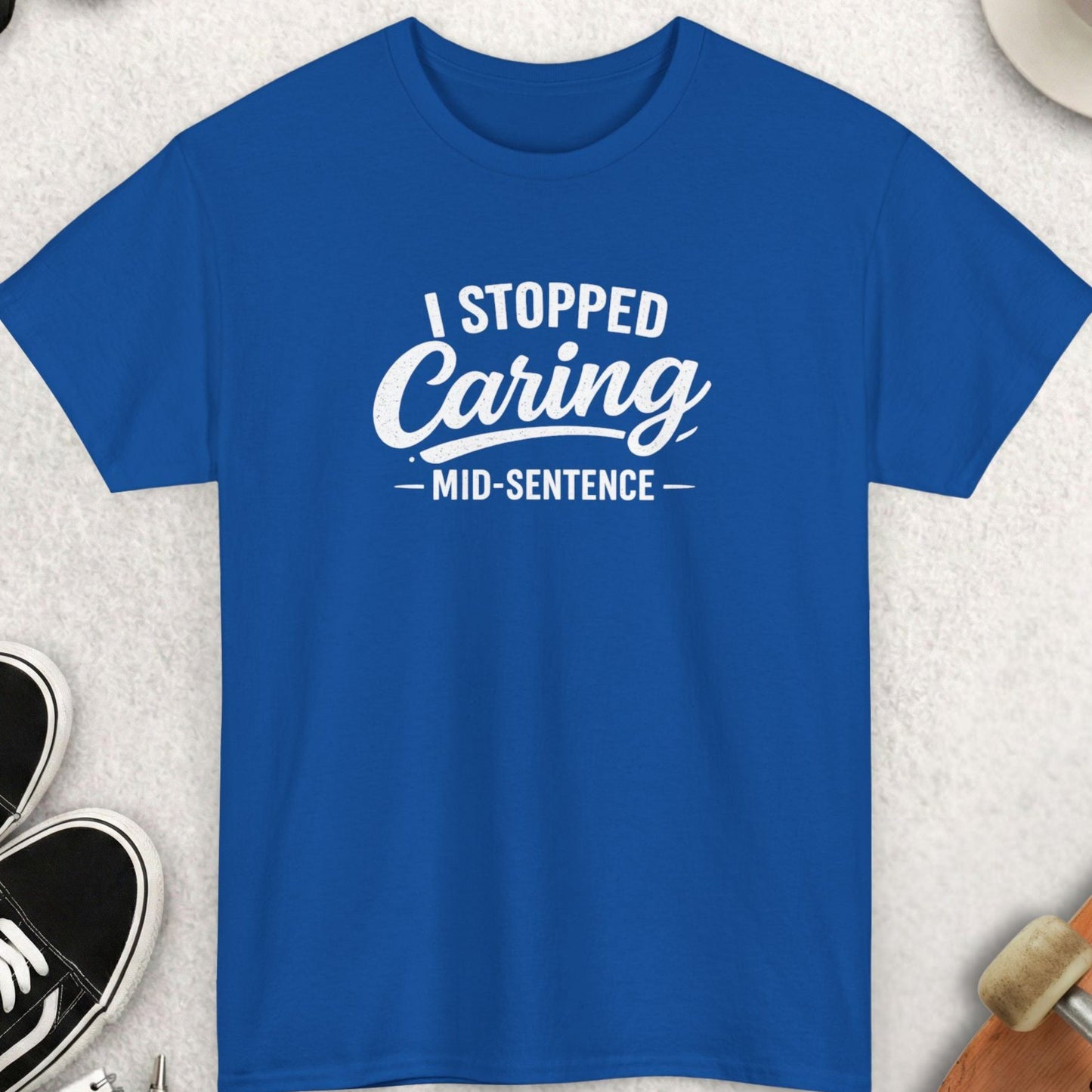Blue t-shirt with 'I Stopped Caring Mid-Sentence' text on a light gray surface with accessories.