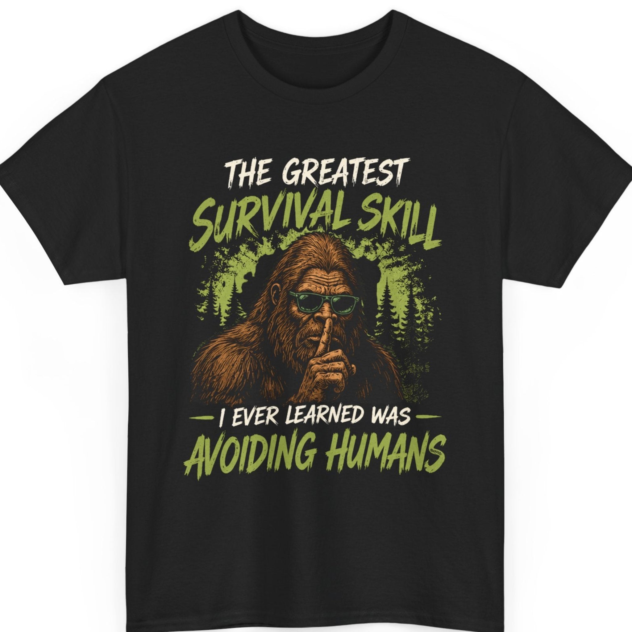 Mayhem Haus Bigfoot graphic t-shirt on a black shirt featuring a detailed Sasquatch wearing green sunglasses and making a "shhh" gesture against a distressed forest backdrop with the quote "The Greatest Survival Skill I Ever Learned Was Avoiding Humans."