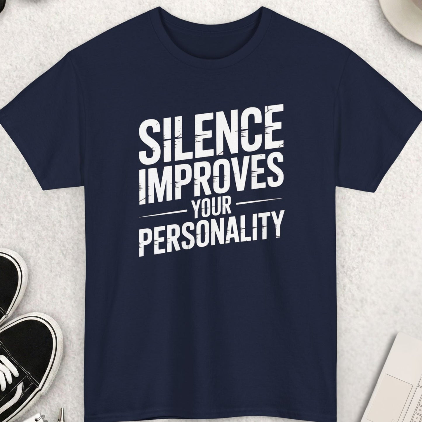 Navy blue t-shirt with 'Silence Improves Your Personality' text on a light gray surface with accessories.