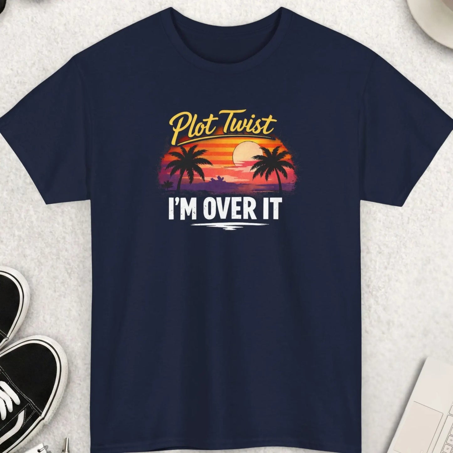 Black t-shirt with 'Plot Twist I'm Over It' design on a light gray surface with accessories.