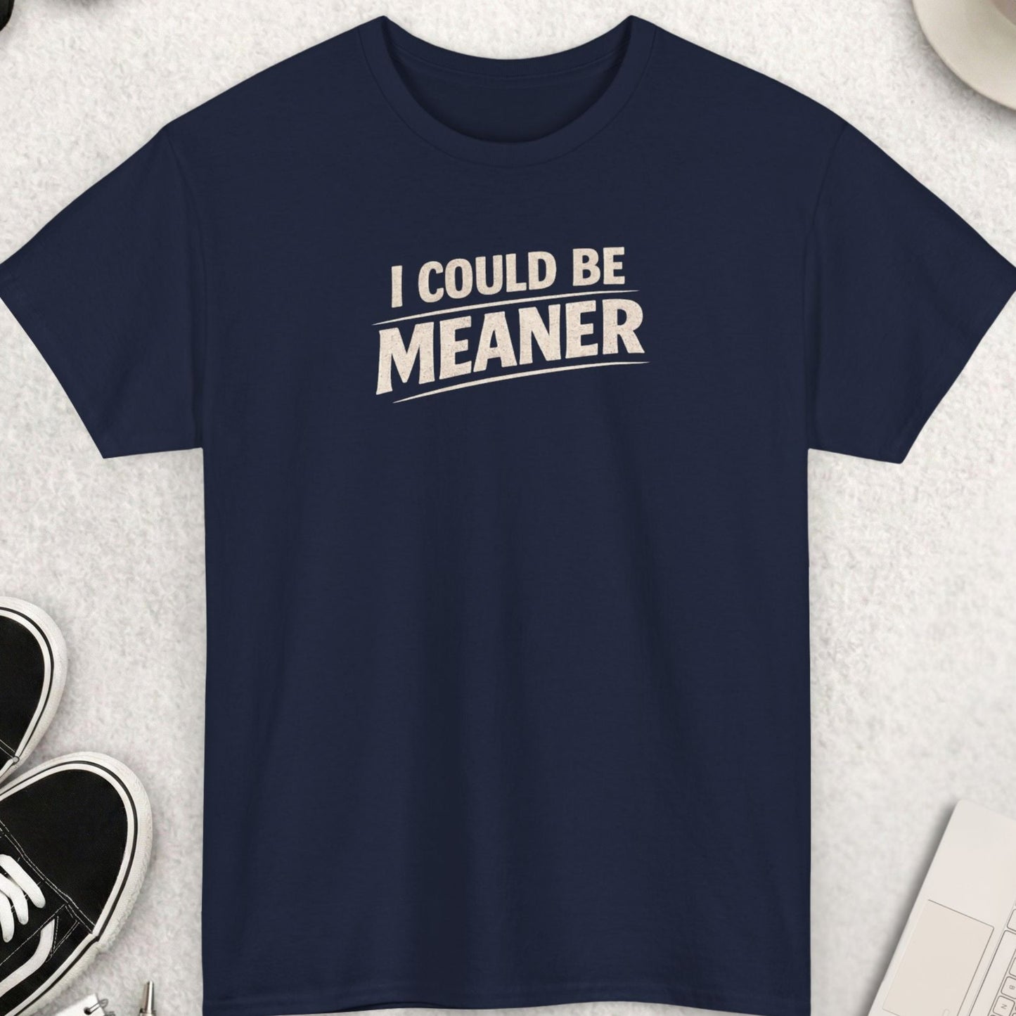Navy blue t-shirt with 'I Could Be Meaner' text on a light gray surface with accessories.
