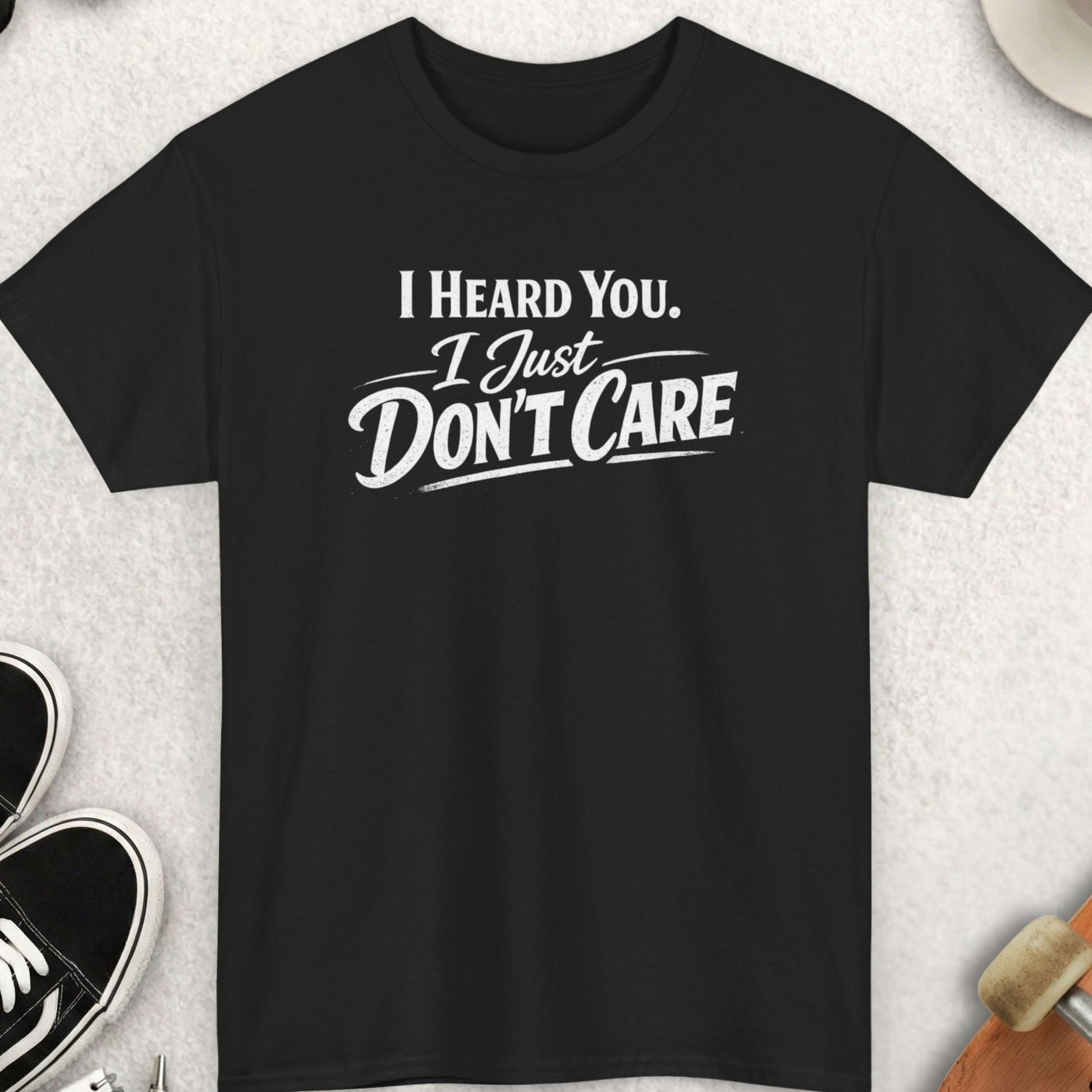 Black t-shirt with 'I Heard You, I Just Don't Care' text on a light gray surface with accessories.