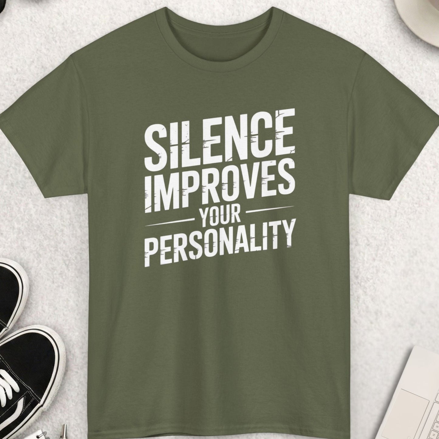 Green t-shirt with 'Silence Improves Your Personality' text on a light gray surface with accessories.