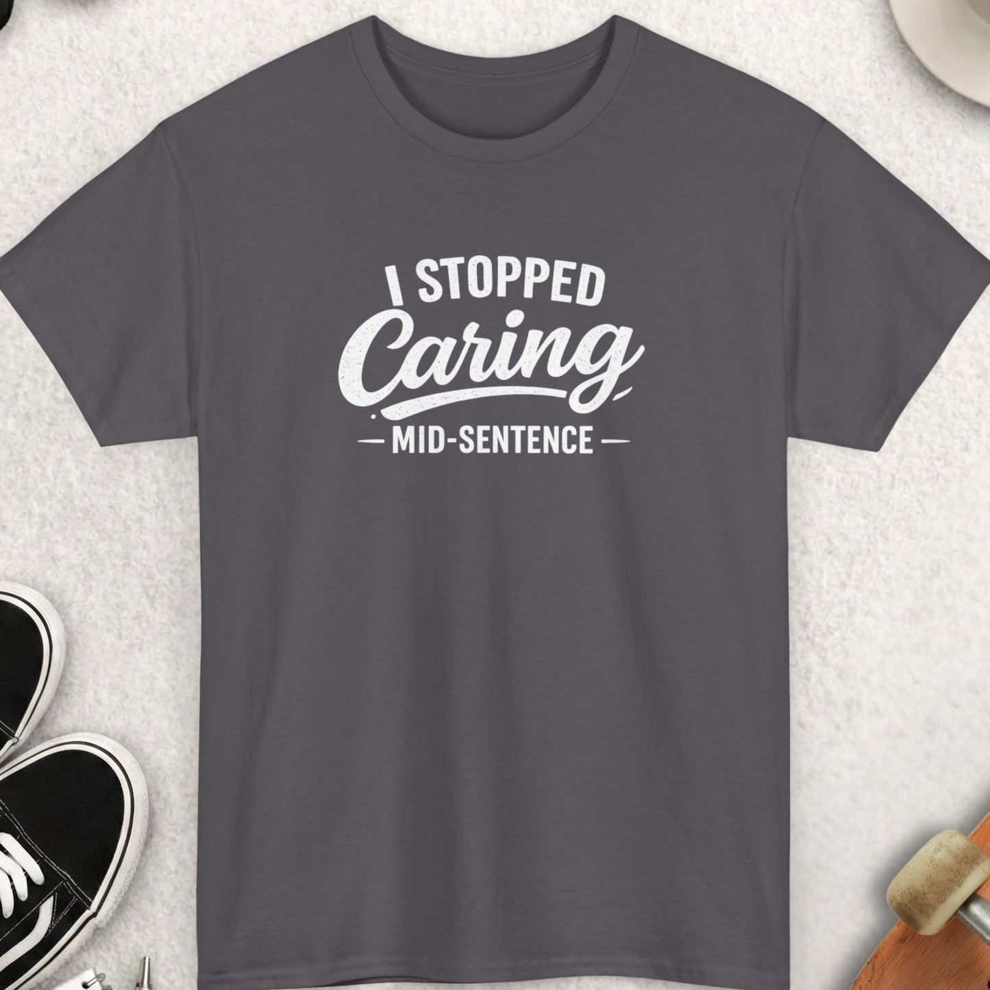 Gray t-shirt with 'I Stopped Caring Mid-Sentence' text on a light gray surface with accessories.