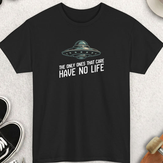 Black t-shirt "The Only Ones That Care Have No Life" with UFO graphic and text on a light gray surface with accessories.