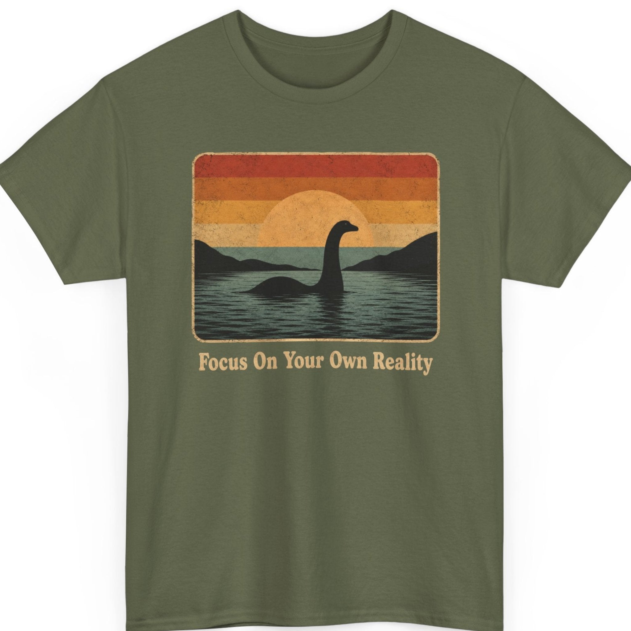 Mayhem Haus vintage Loch Ness shirt on a military green shirt featuring a minimalist silhouette of Nessie in a peaceful lake beneath a distressed retro sunset with the phrase "Focus On Your Own Reality."