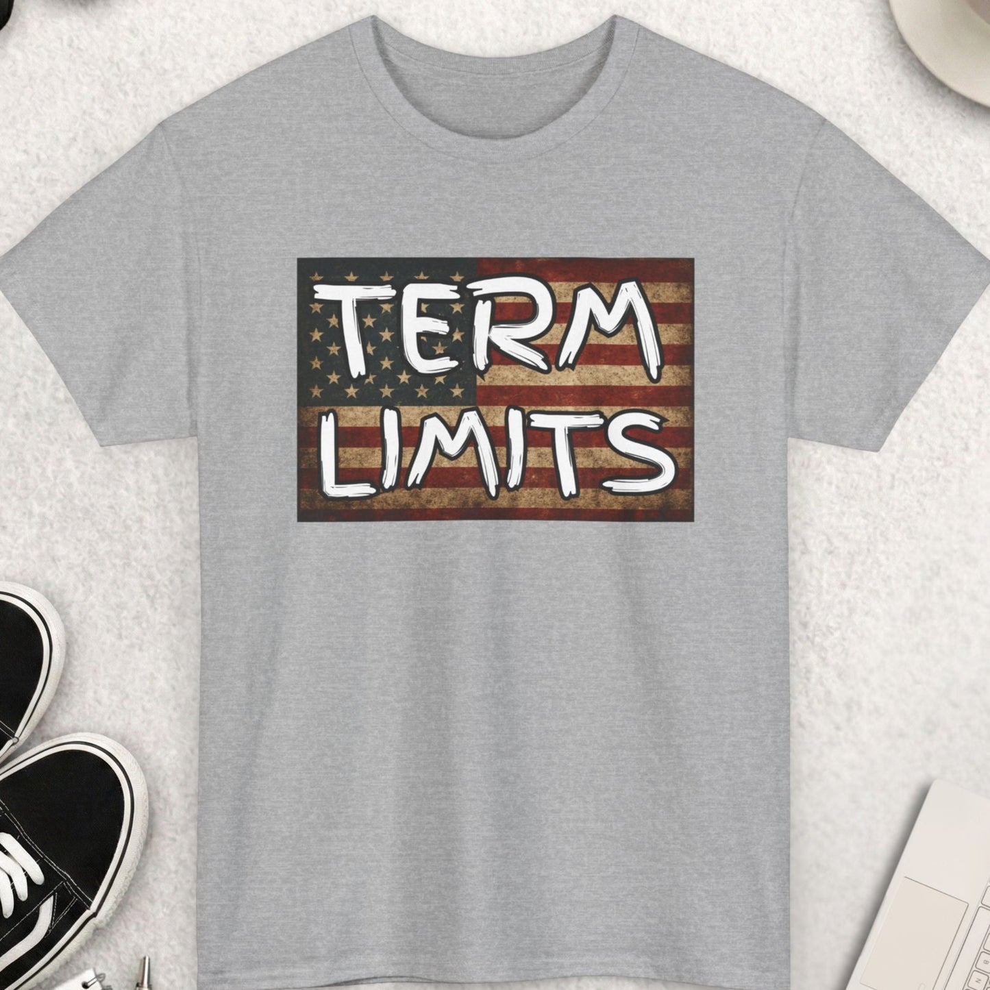Gray t-shirt with 'TERM LIMITS' graphic on a light surface with shoes, coffee, and accessories.
