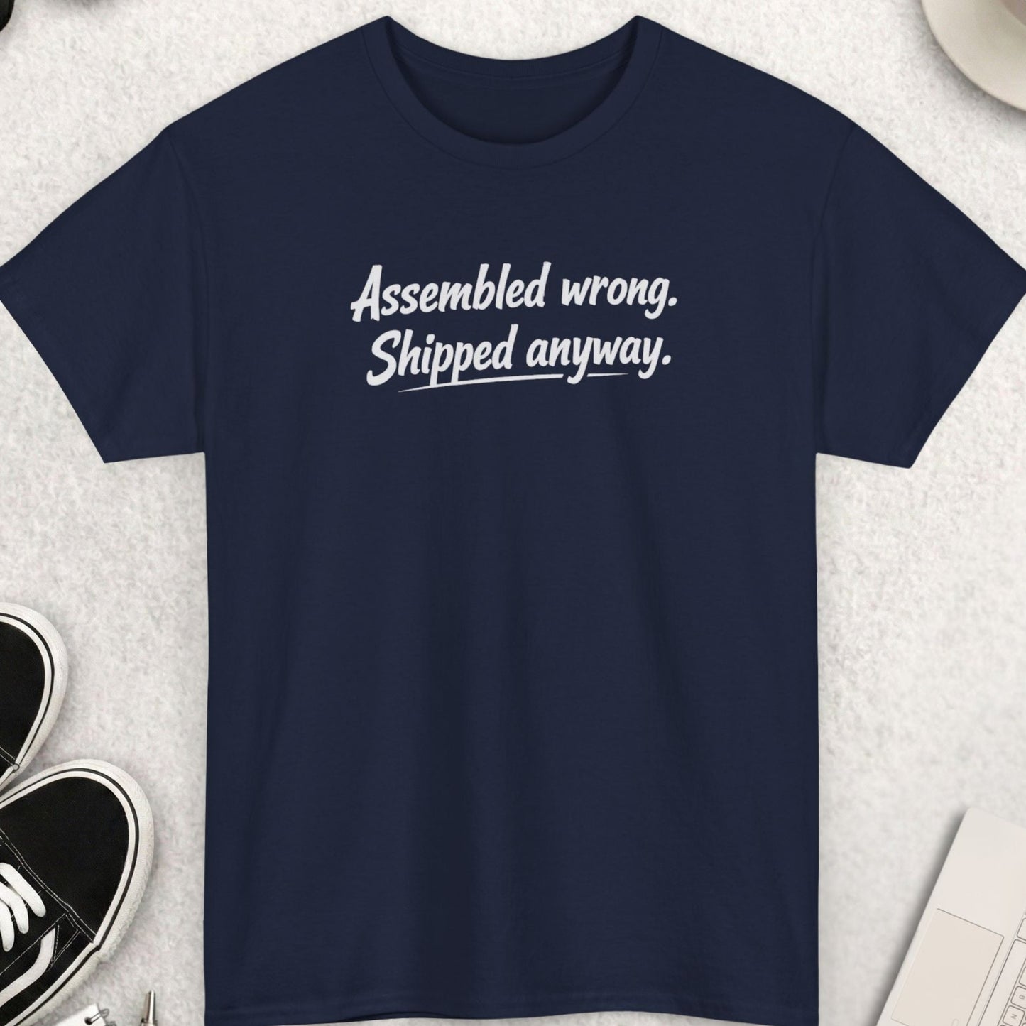 Navy blue t-shirt with text on a light gray surface with shoes, coffee, and accessories.