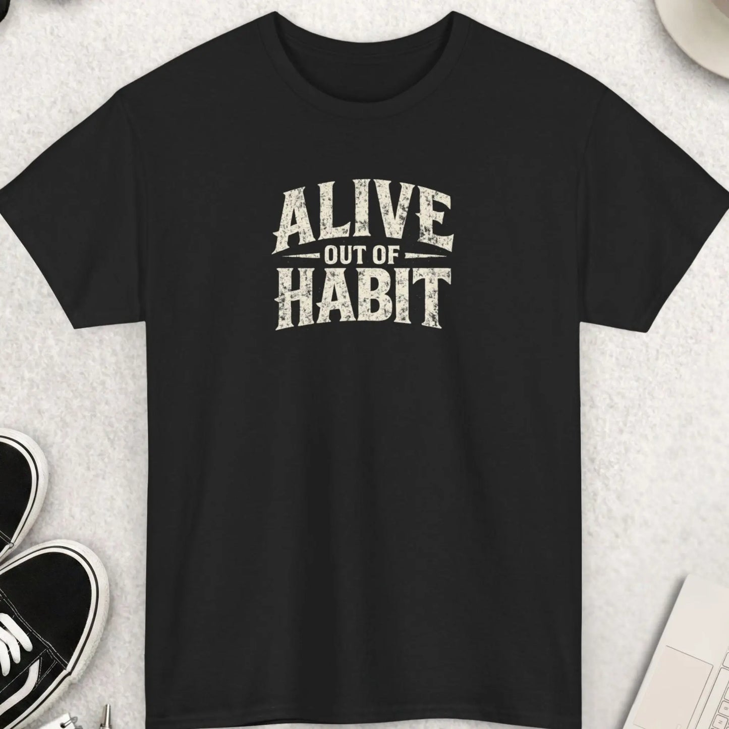 Black distressed typography graphic t-shirt featuring the phrase “Alive Out Of Habit” in large vintage grunge cream lettering with a dark humor streetwear aesthetic by Mayhem Haus.