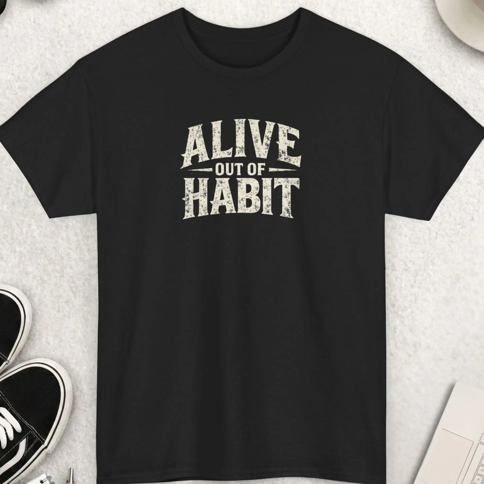 Black distressed typography graphic t-shirt featuring the phrase “Alive Out Of Habit” in large vintage grunge cream lettering with a dark humor streetwear aesthetic by Mayhem Haus.