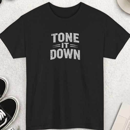 Black t-shirt with 'TONE IT DOWN' text on a light gray surface with shoes, coffee, and accessories.