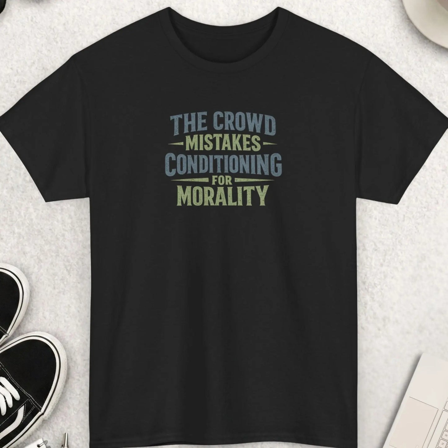 Black t-shirt featuring distressed vintage typography reading “The Crowd Mistakes Conditioning For Morality” in muted earth-tone colors with a bold minimalist layout.