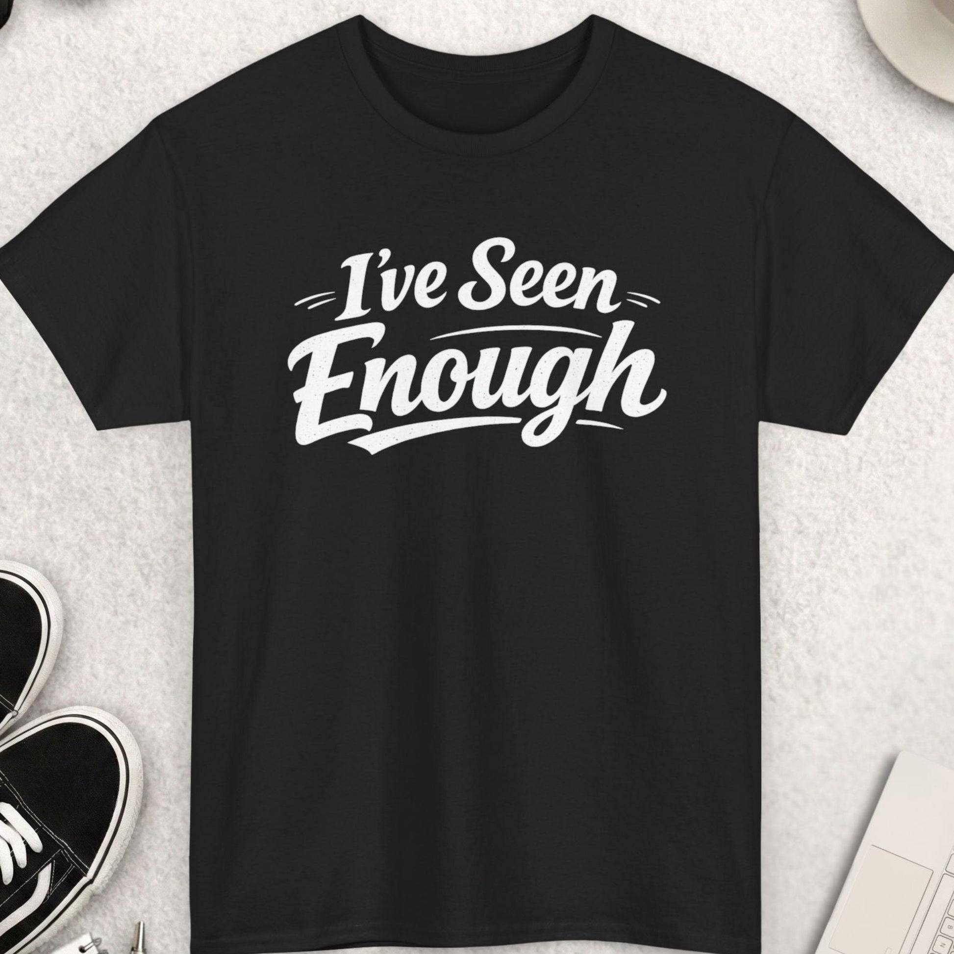 Black t-shirt with 'I've Seen Enough' text on a light gray surface with accessories.