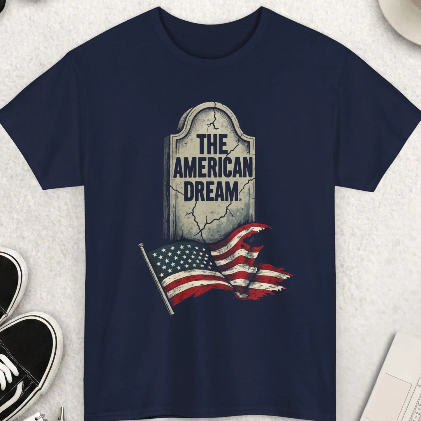 Navy blue t-shirt with 'The American Dream' graphic on a light gray surface with accessories.