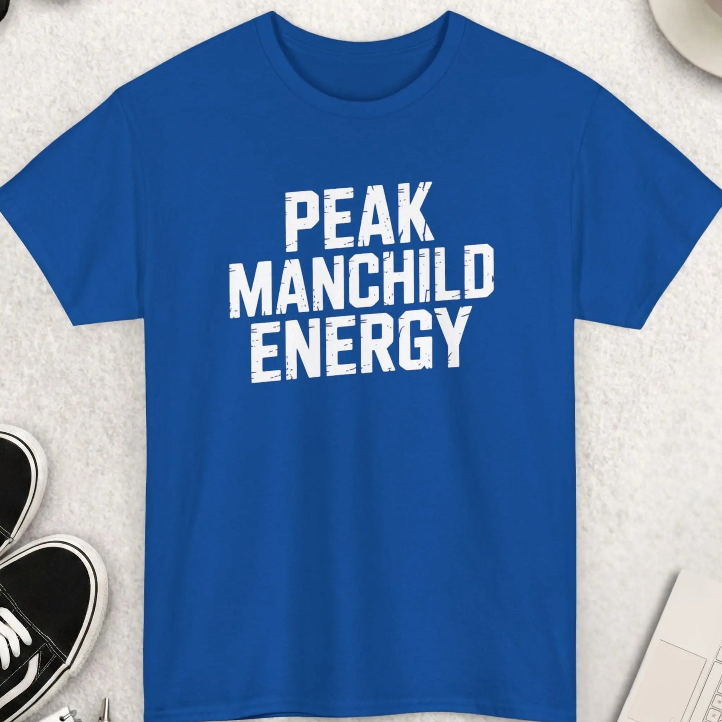 Blue t-shirt with 'PEAK MANCHILD ENERGY' text on a light gray surface with accessories.