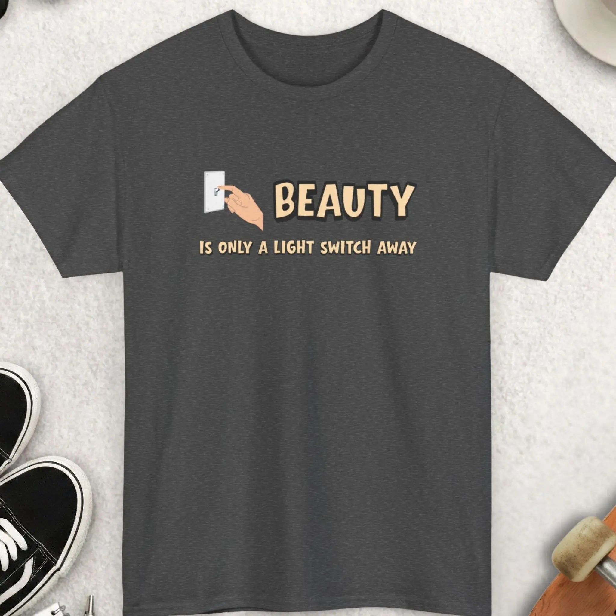 Gray t-shirt with 'Beauty is only a light switch away' text on a light gray surface with accessories.