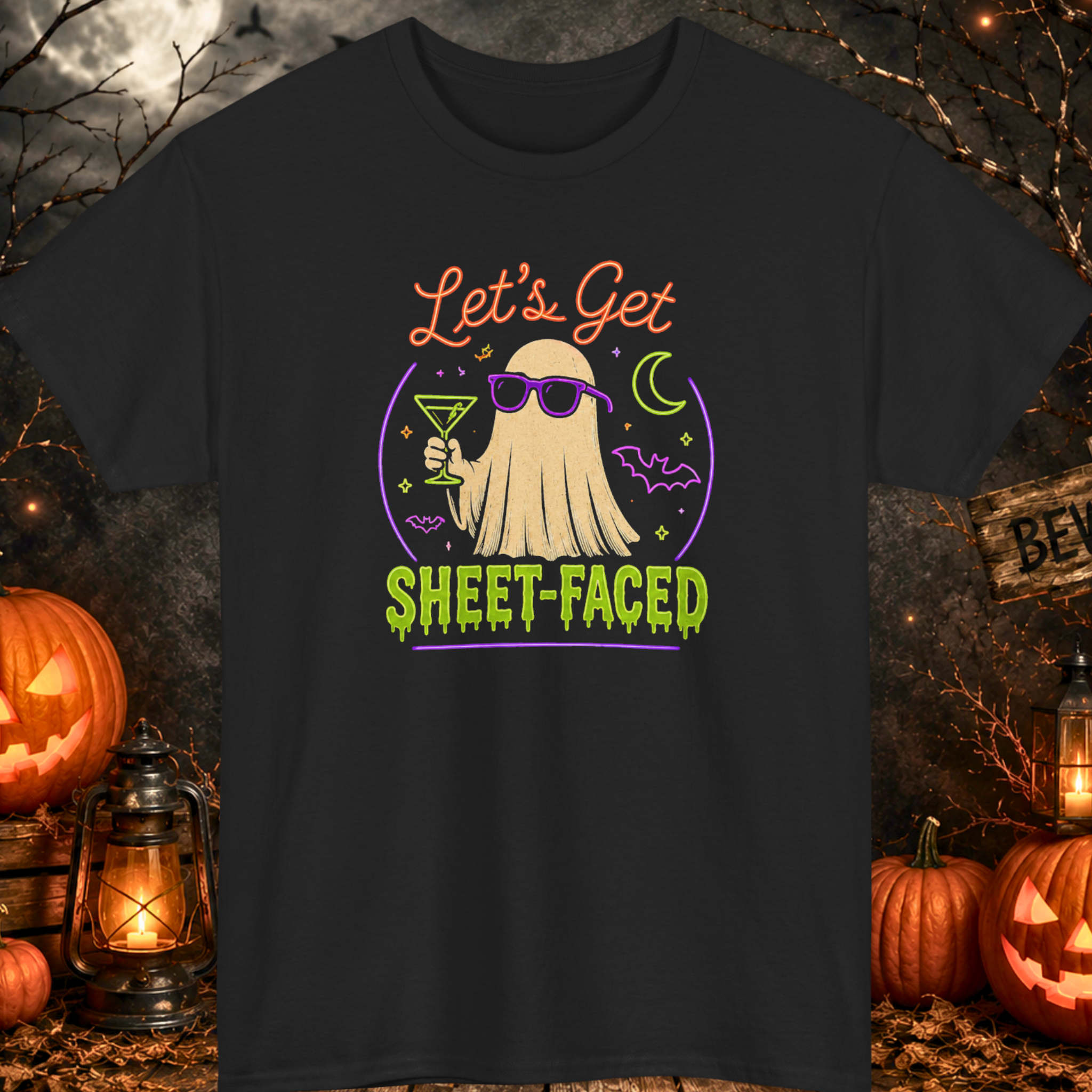 Mayhem Haus Halloween t-shirt on a black shirt featuring a stylish ghost wearing sunglasses while holding a cocktail, surrounded by bats, stars, and a crescent moon above the phrase, “Let's Get Sheet-Faced,” in bright neon-inspired lettering.