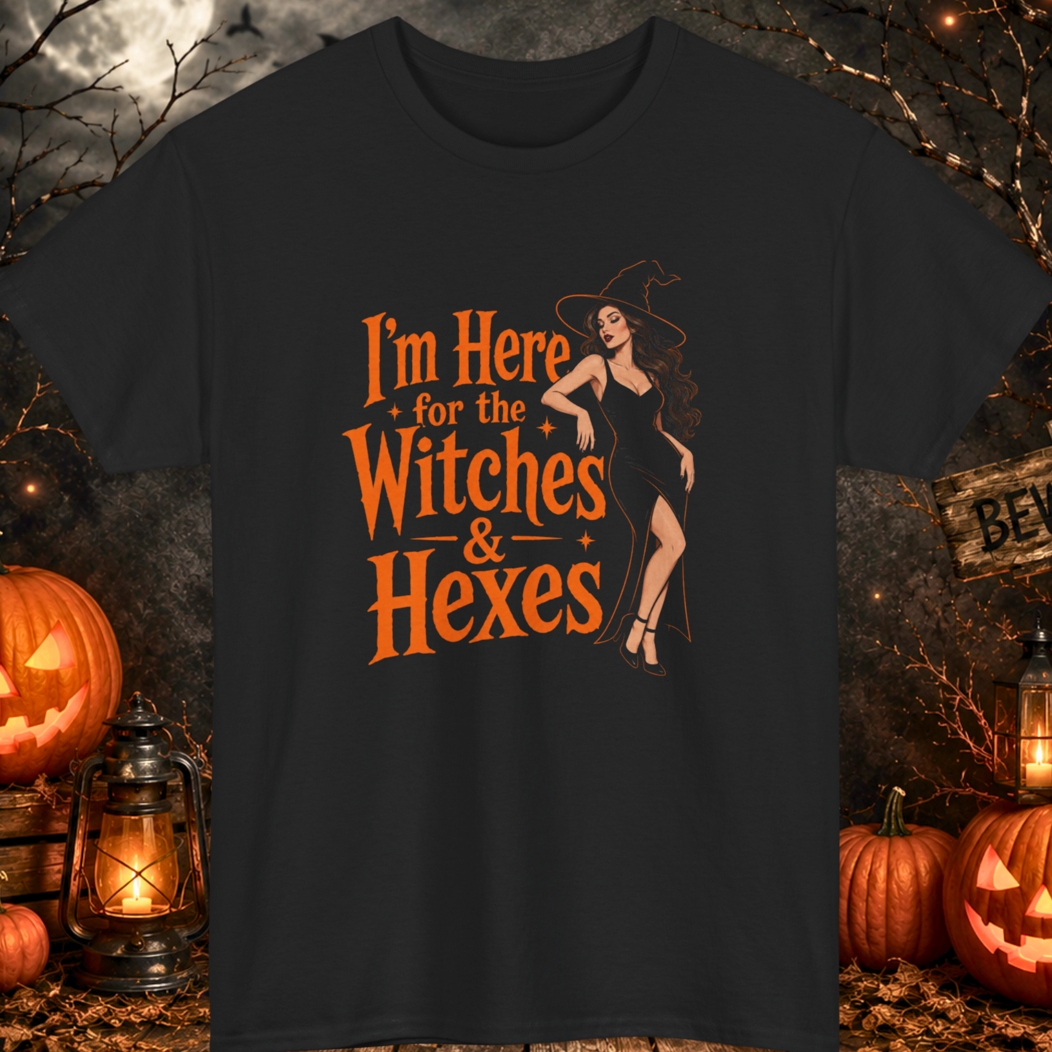 Mayhem Haus Halloween graphic t-shirt on a black shirt featuring a stylish witch in a sleek black dress and pointed hat beside bold orange typography reading "I'm Here for the Witches & Hexes."