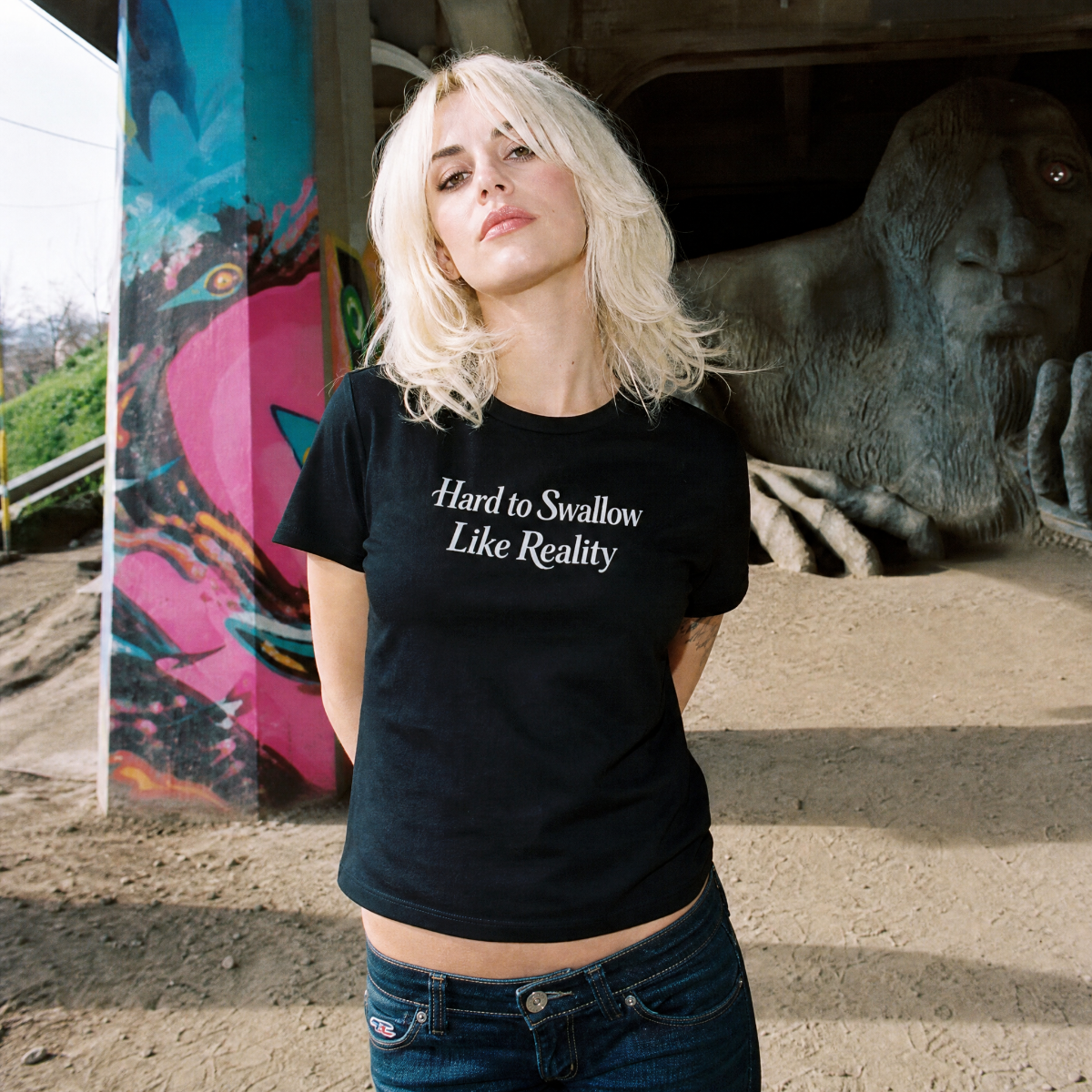 Mayhem Haus Hard to Swallow Like Reality T-Shirt on a person in front of a painted pillar and sculpture